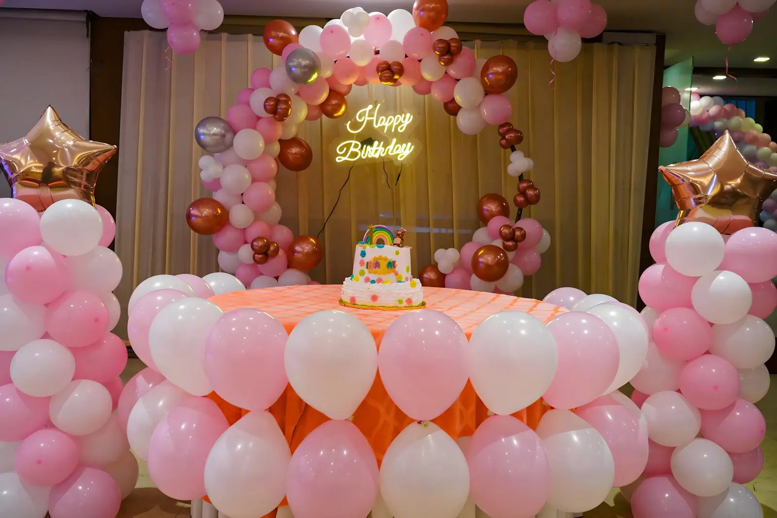 Birthday party setup with a pink balloon arch and cake table