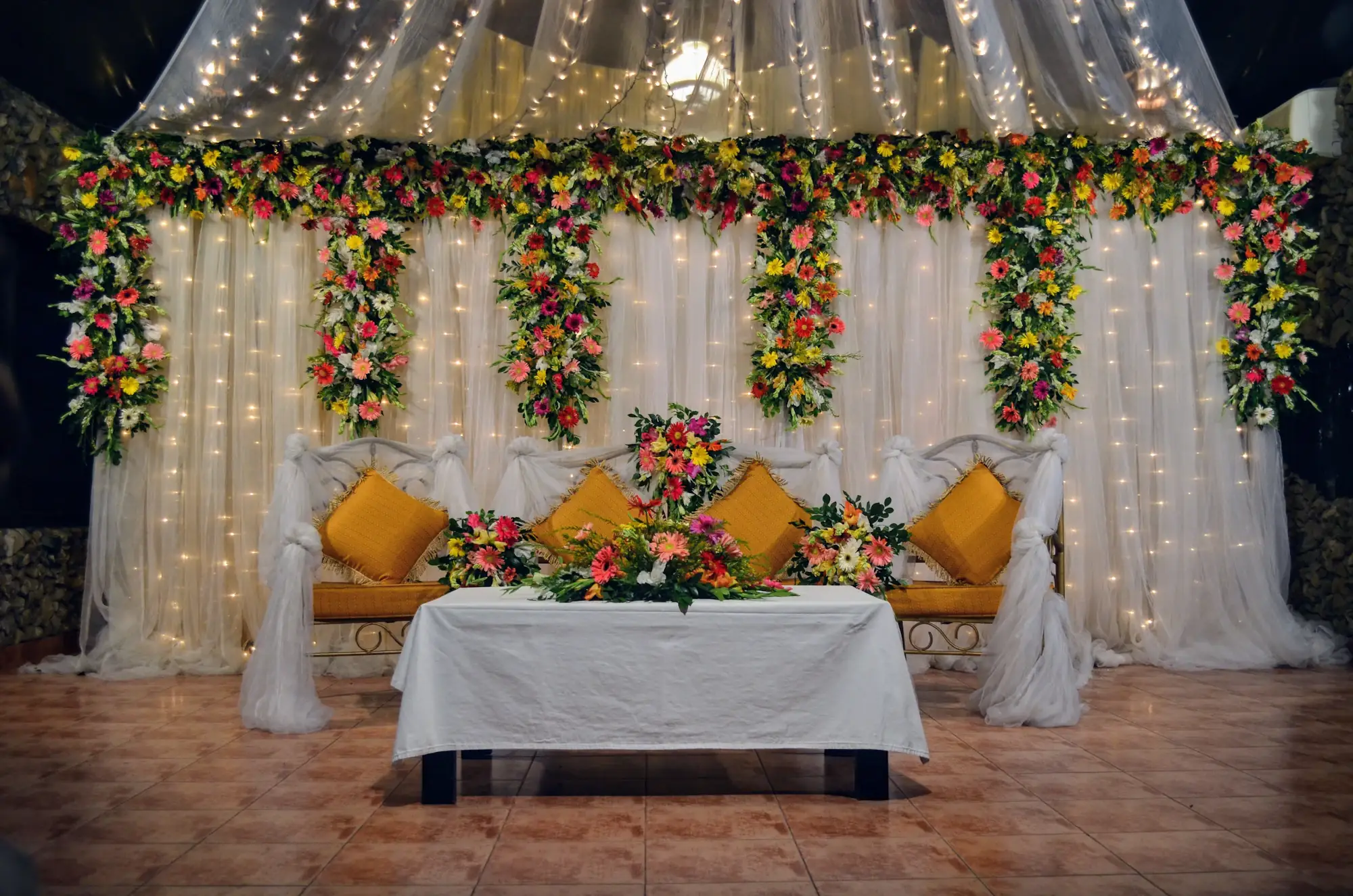 White floral wedding stage with fairy lights and a flower covered sofa